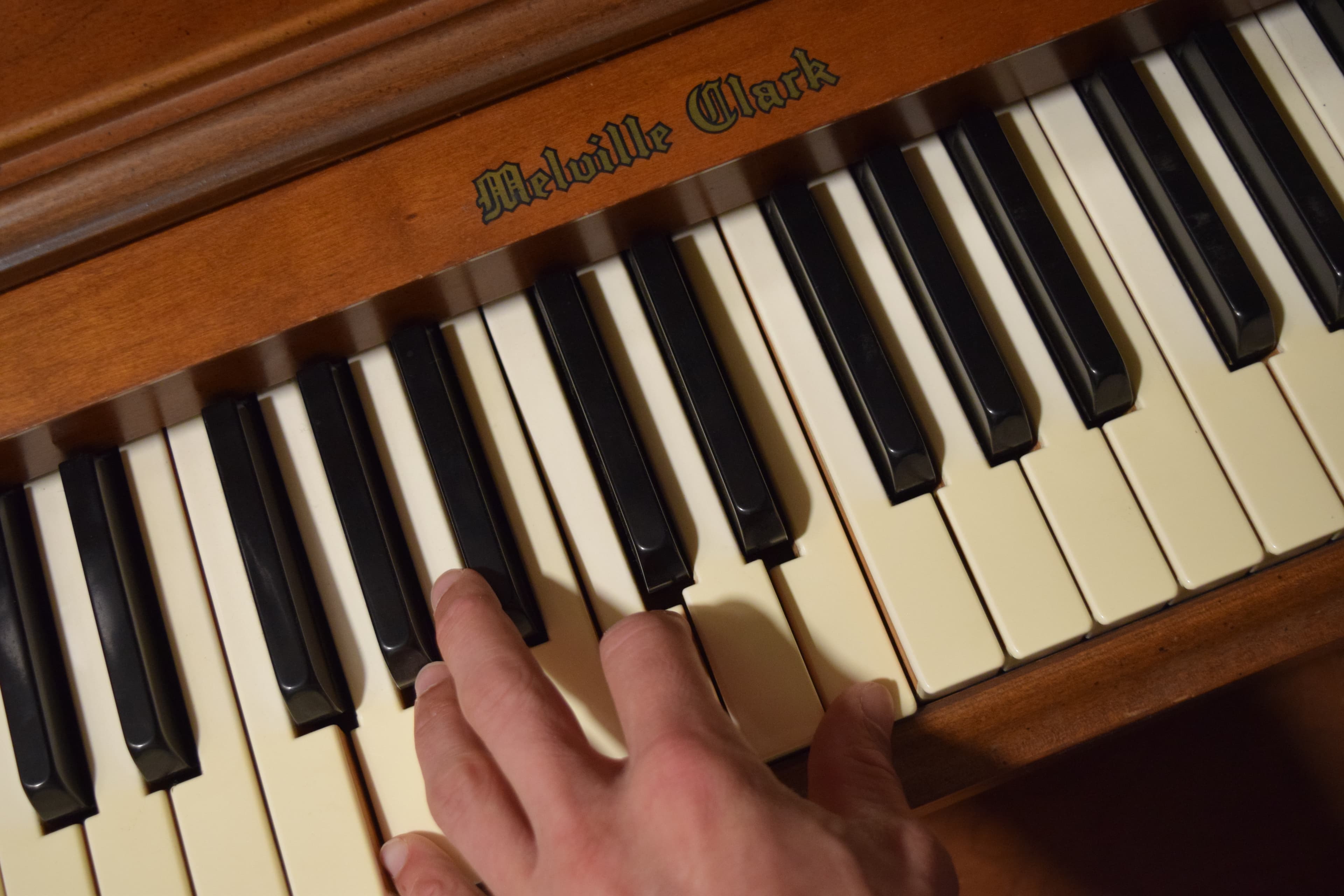 A hand playing chords on an upright piano